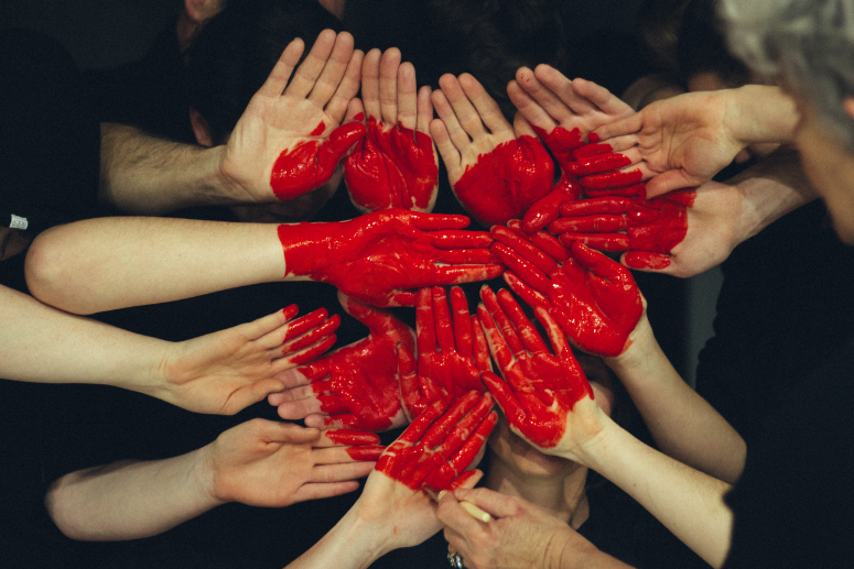 Many hands come together with a painted red heart.