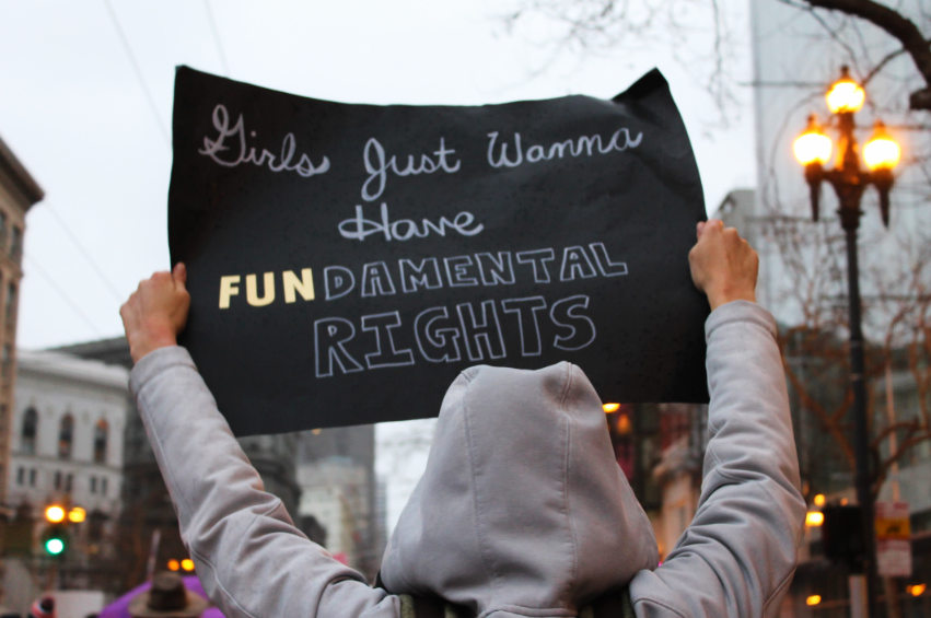 At a rally, a person in a gray hoodie holds up a sign that reads, "Girls just wanna have fundamental rights."